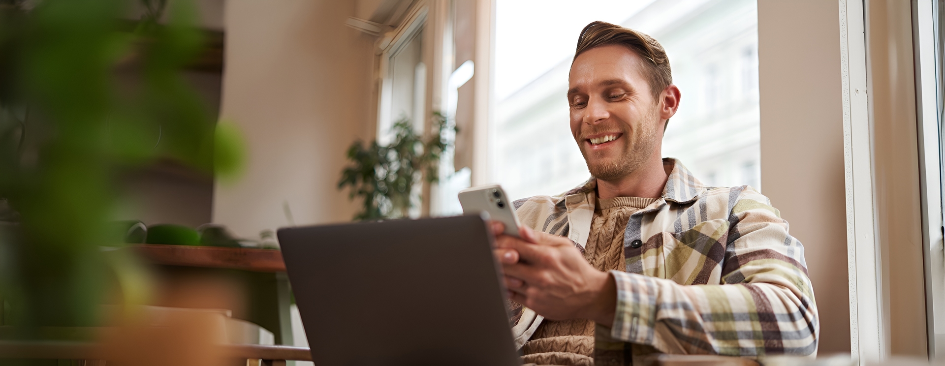 Empreendedor sorrindo ao usar o celular e o notebook em um café
